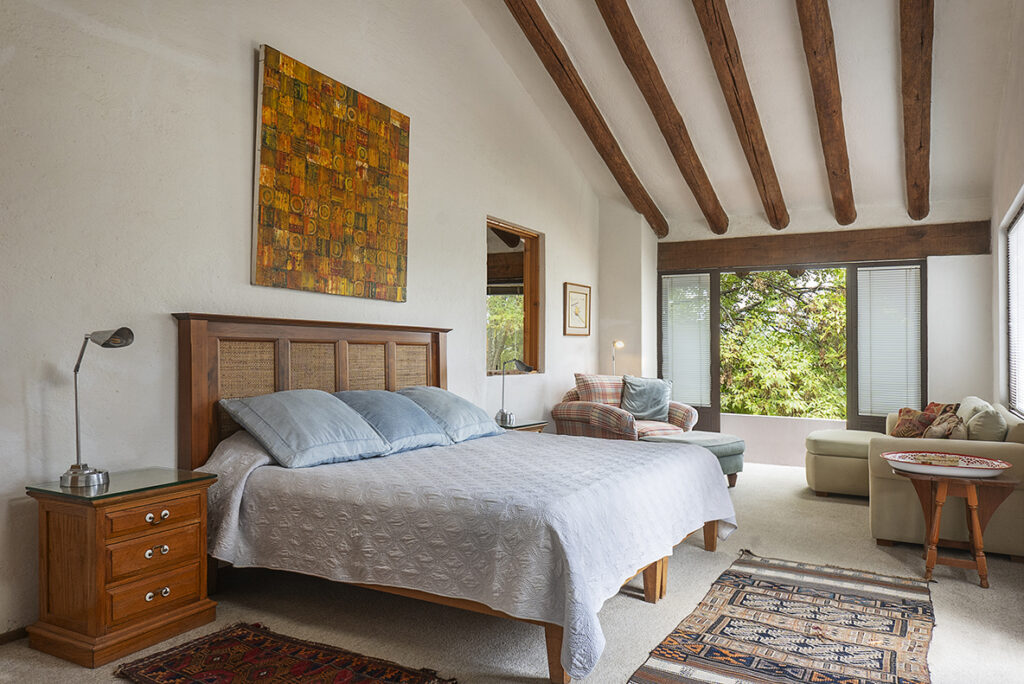 recamara matrimonial con ventana al bosque, dos sillones y un techo alto con vigas de madera  en casa en Valle de bravo, renta vacacional, fotografía profesional